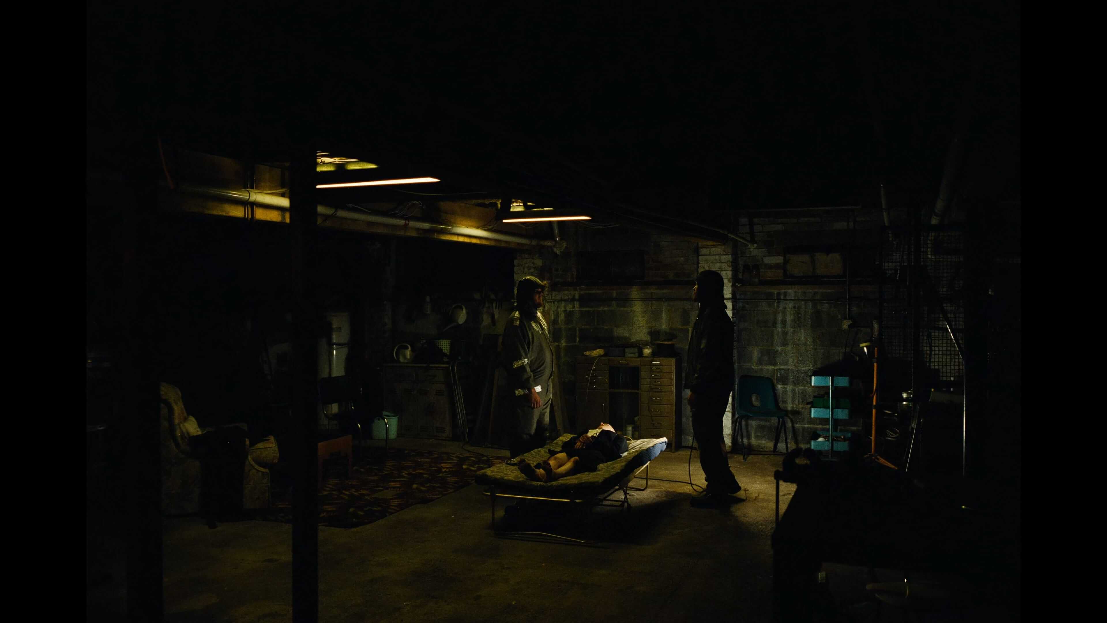 Два мужчины склонились над женщиной на раскладушке в подвале дома