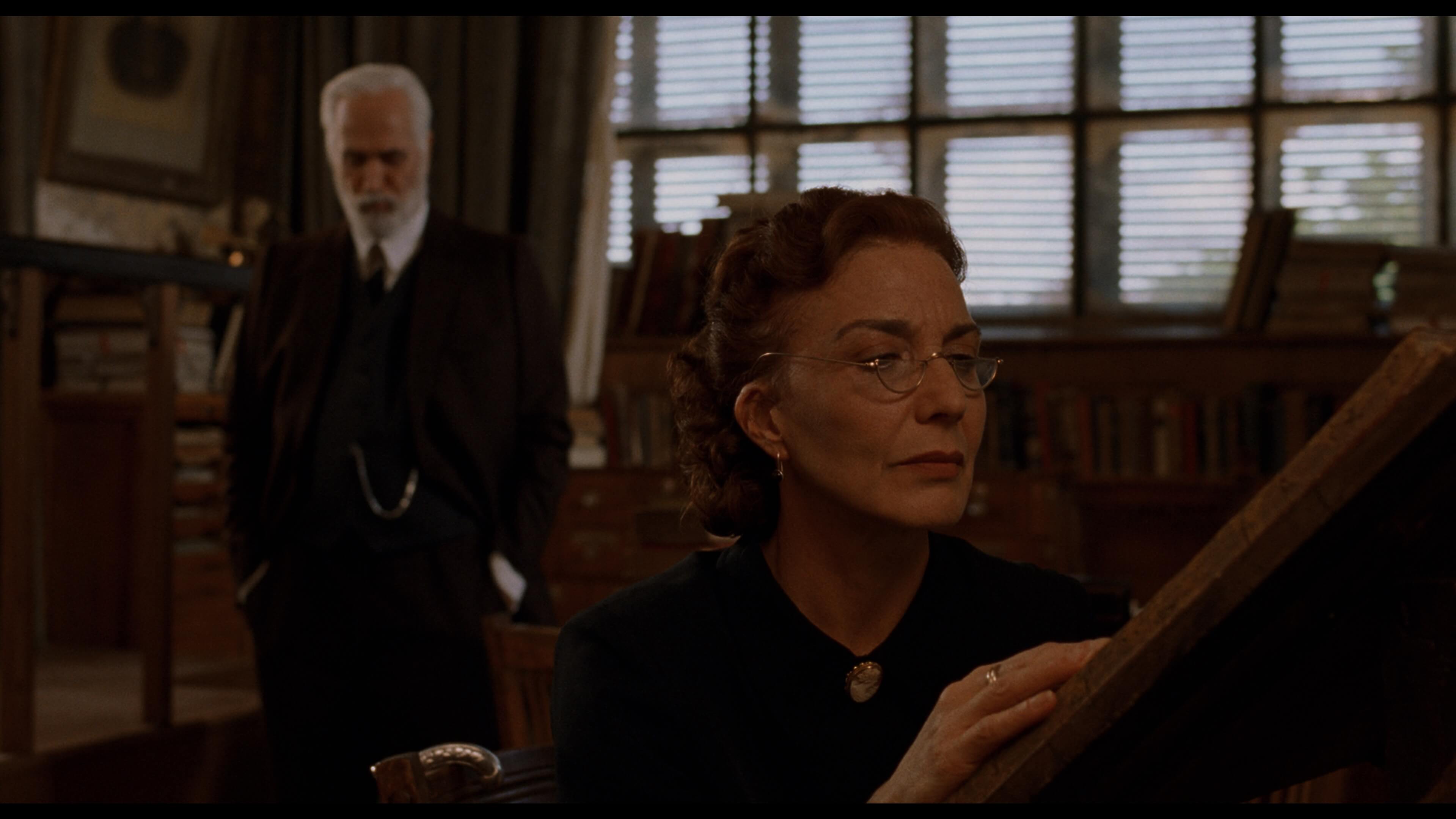 женщина в очках читает книгу, мужчина смотрит на нее